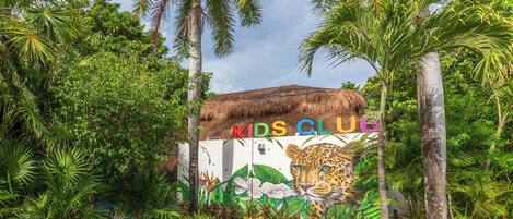 Una entrada con temática tropical que presenta un mural de un leopardo y las palabras 'KIDS CLUB' en un edificio.