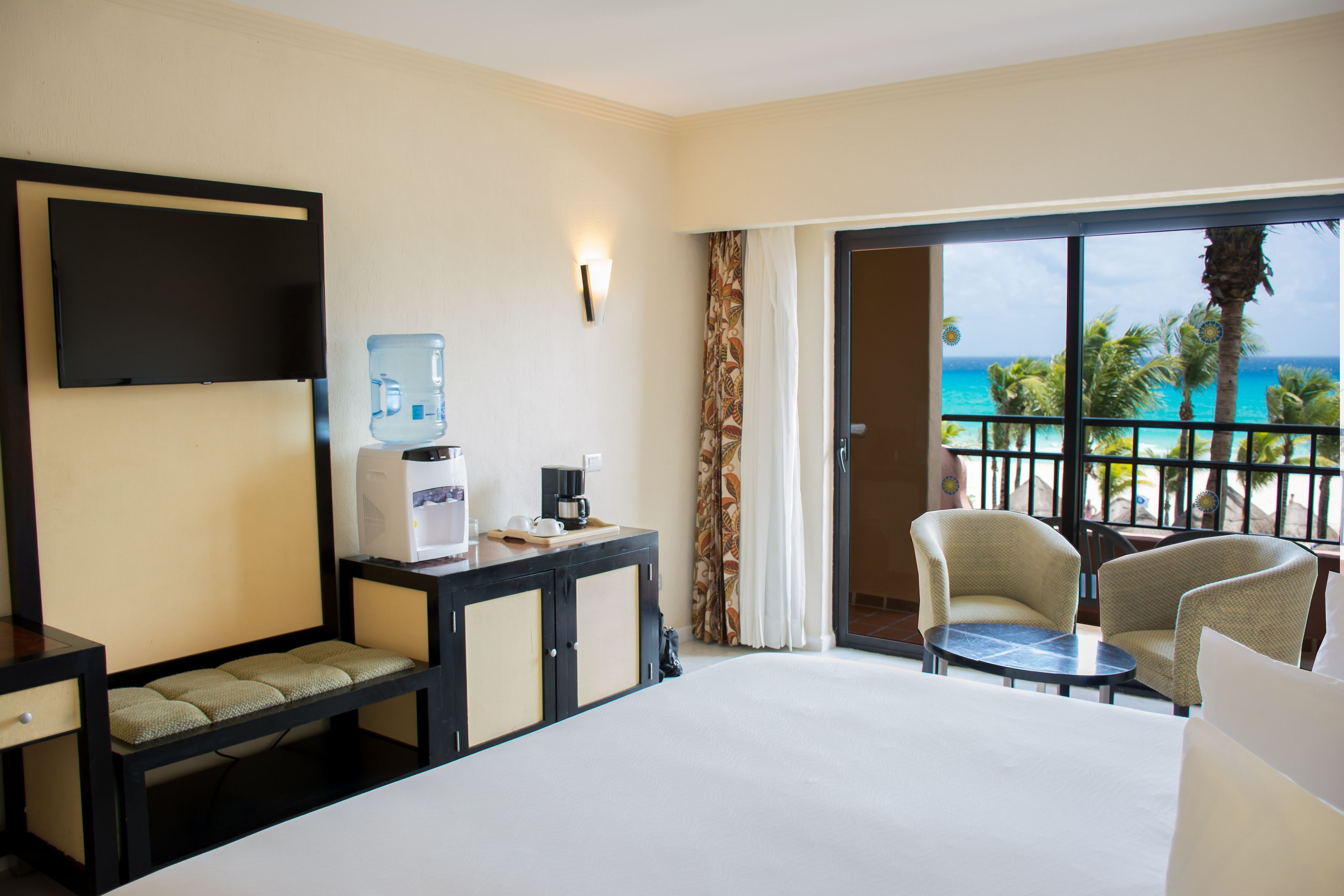 Quarto de hotel com cama, escrivaninha com dispensador de água, cafeteira e vista para o oceano.