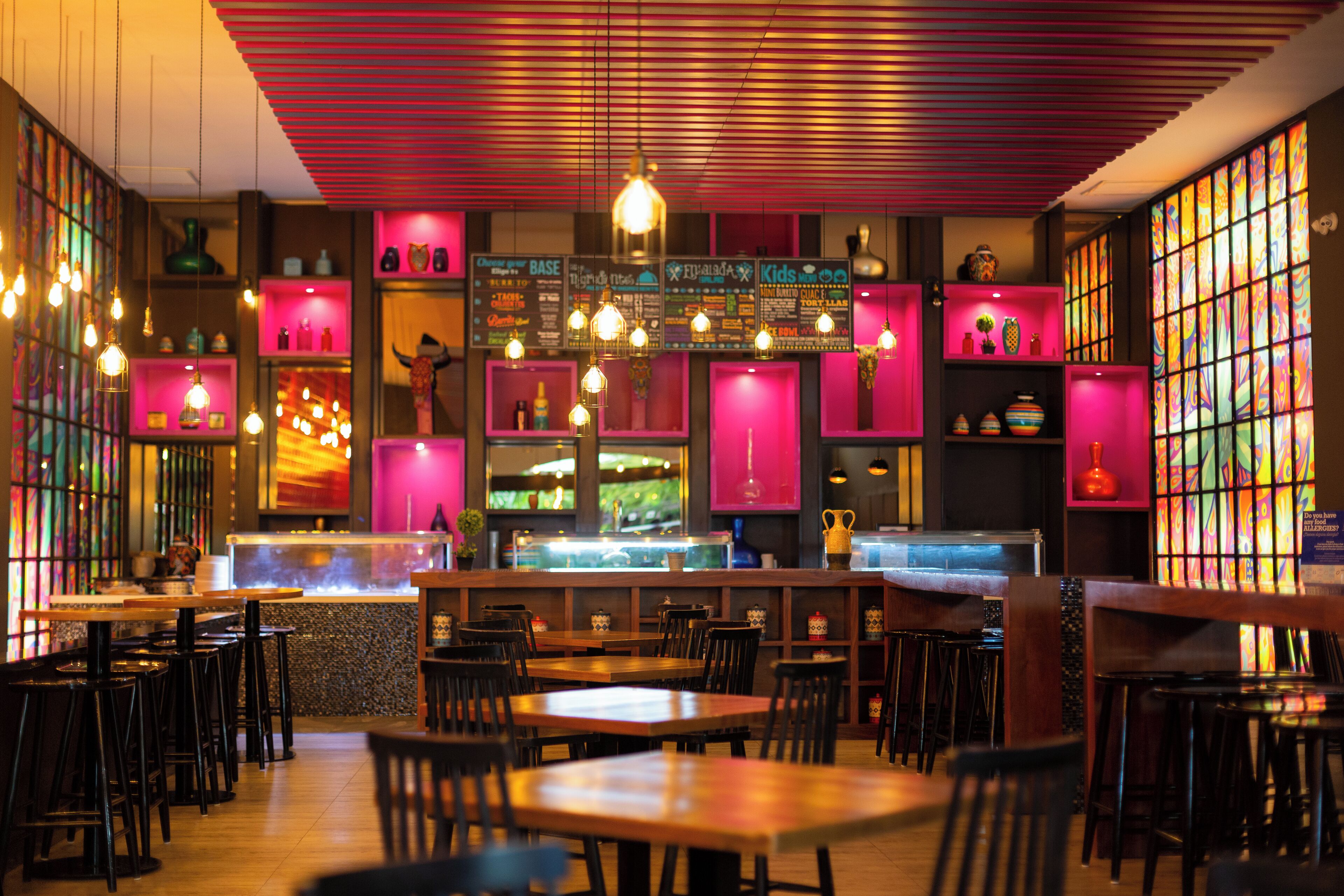A restaurant interior with wooden tables and chairs, hanging light fixtures, and colorful wall decorations.