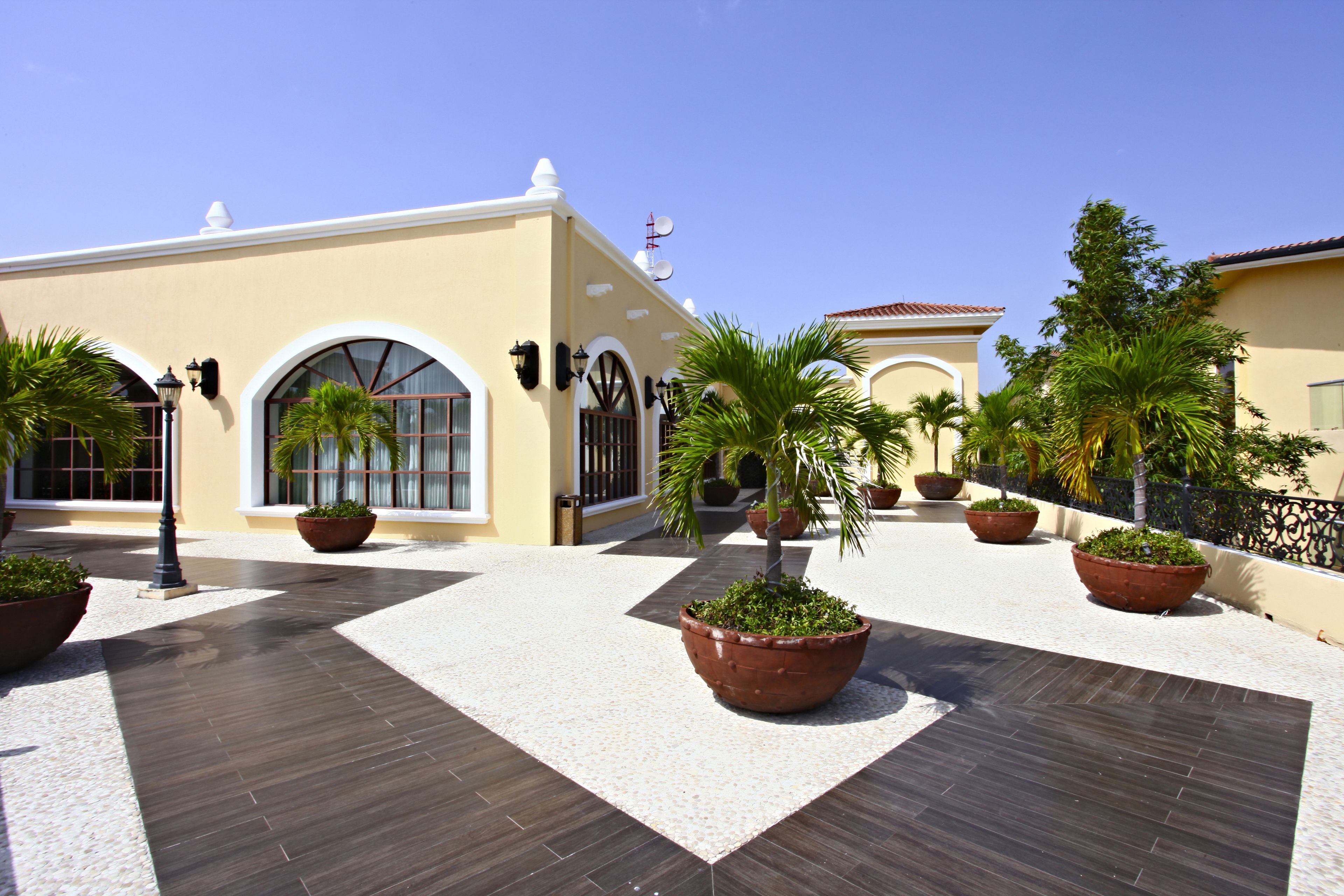 Un patio con piso de baldosas, plantas en macetas y un edificio con ventanas arqueadas y tejado de tejas.
