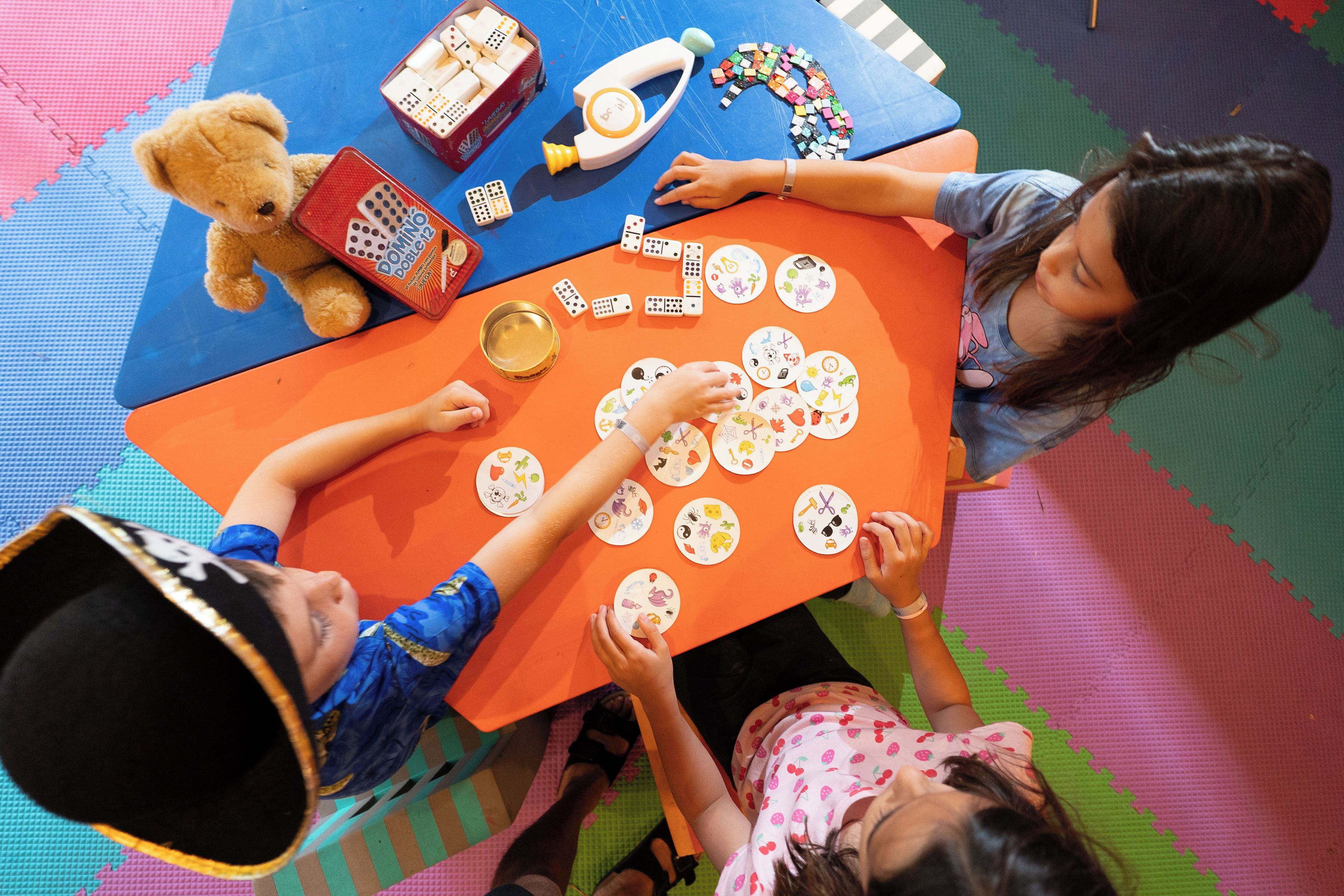 A group of children playing with dominoes and other toys at a table.