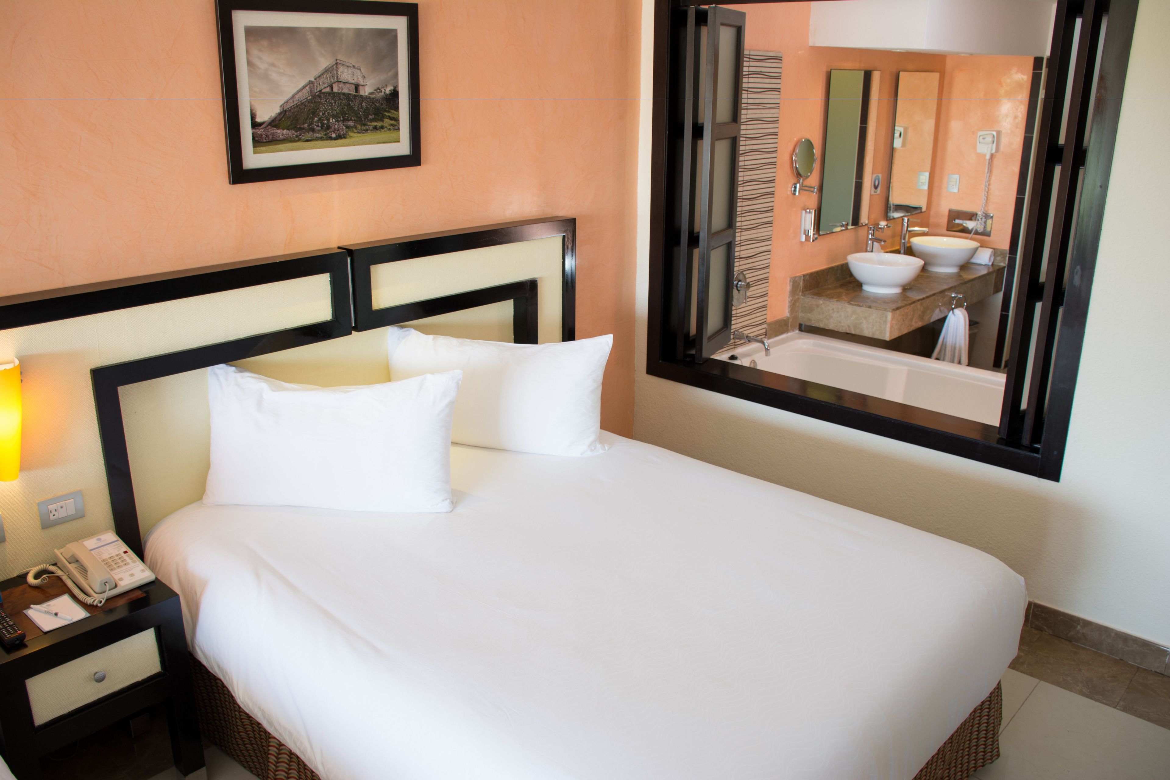 Une chambre d’hôtel avec un grand lit, un téléphone sur la table de chevet et une salle de bain visible à travers une porte ouverte.