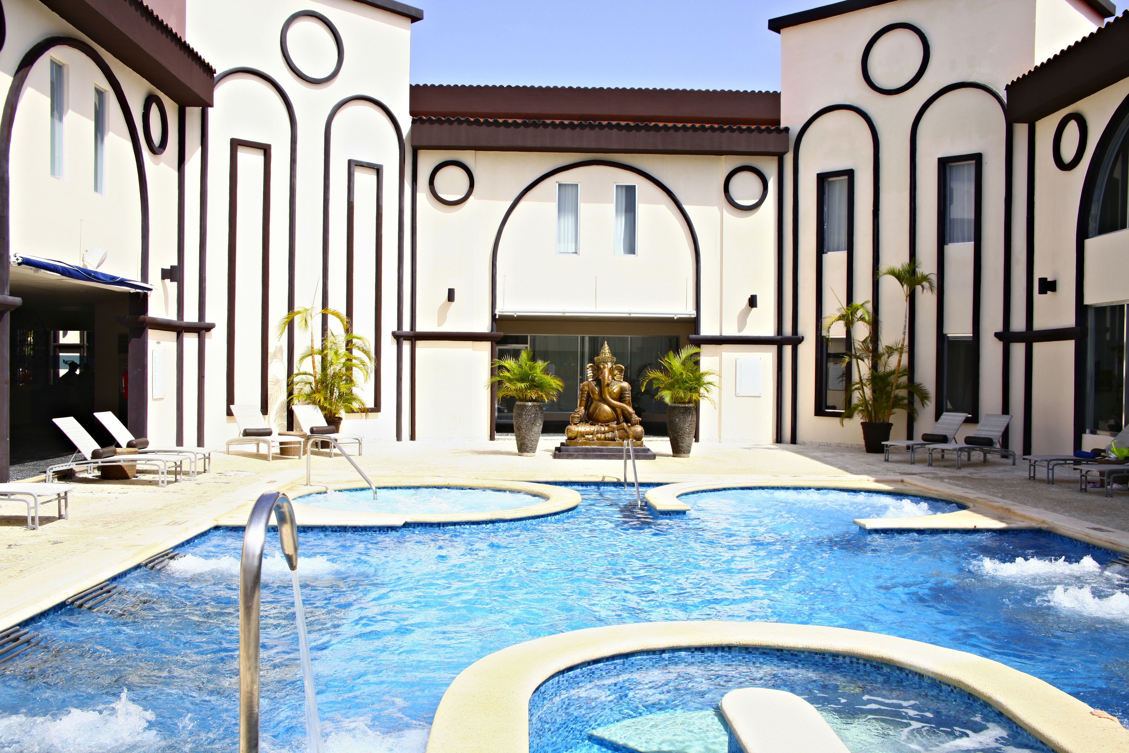 A swimming pool with a Buddha statue, lounge chairs, and potted plants.