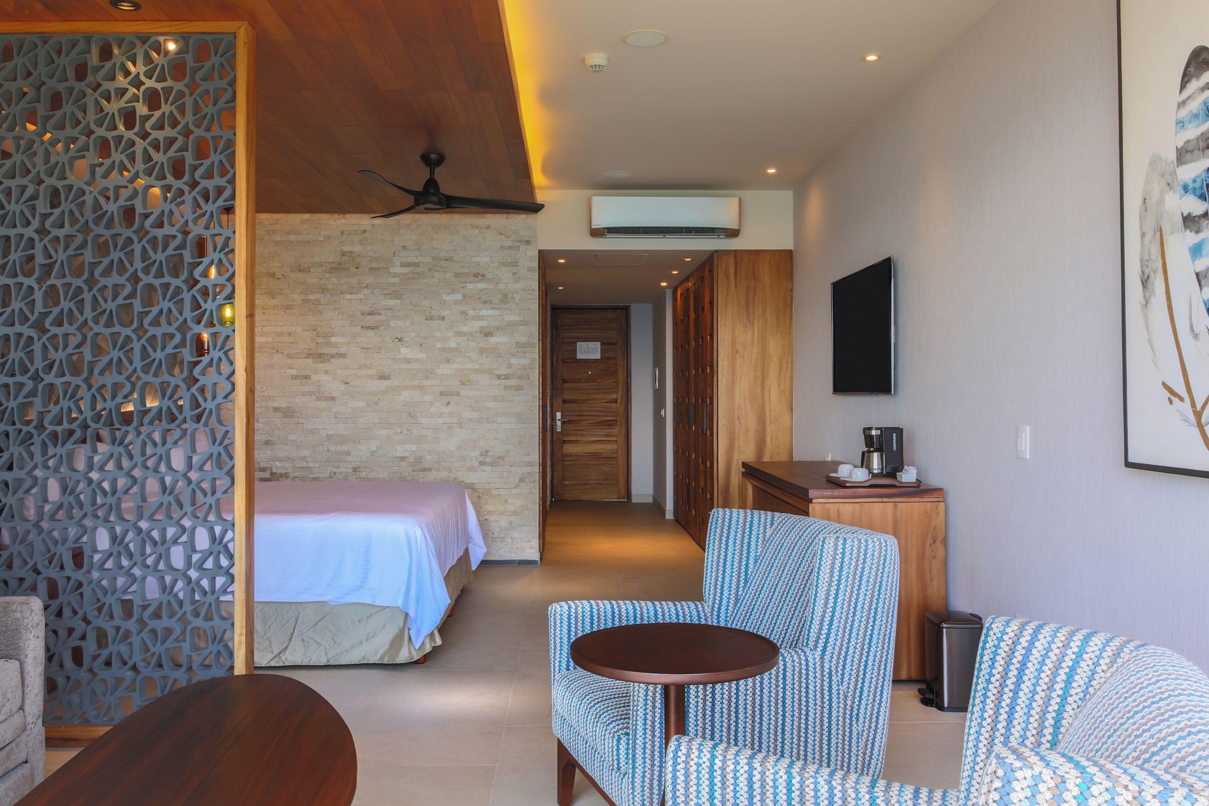 A hotel room with a bed, a desk, a chair, a small table, and a TV mounted on the wall.
