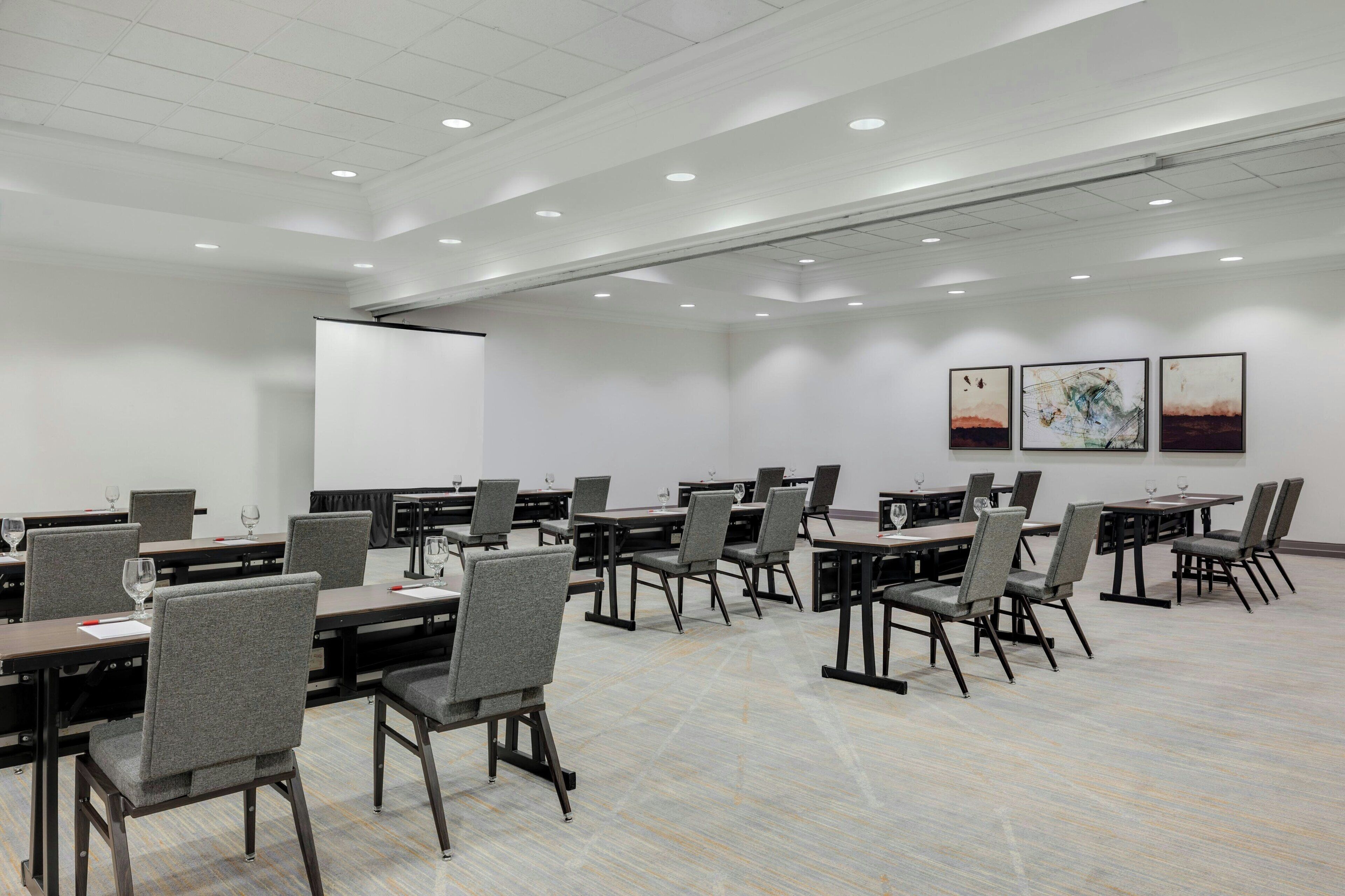 A conference room with multiple tables and chairs, white walls, and ceiling lights.