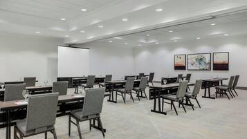 A conference room with multiple tables and chairs, white walls, and ceiling lights.