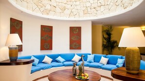 Een moderne woonkamer met een blauwe bank, een ronde houten salontafel met fruit, en decoratieve wandkunst.