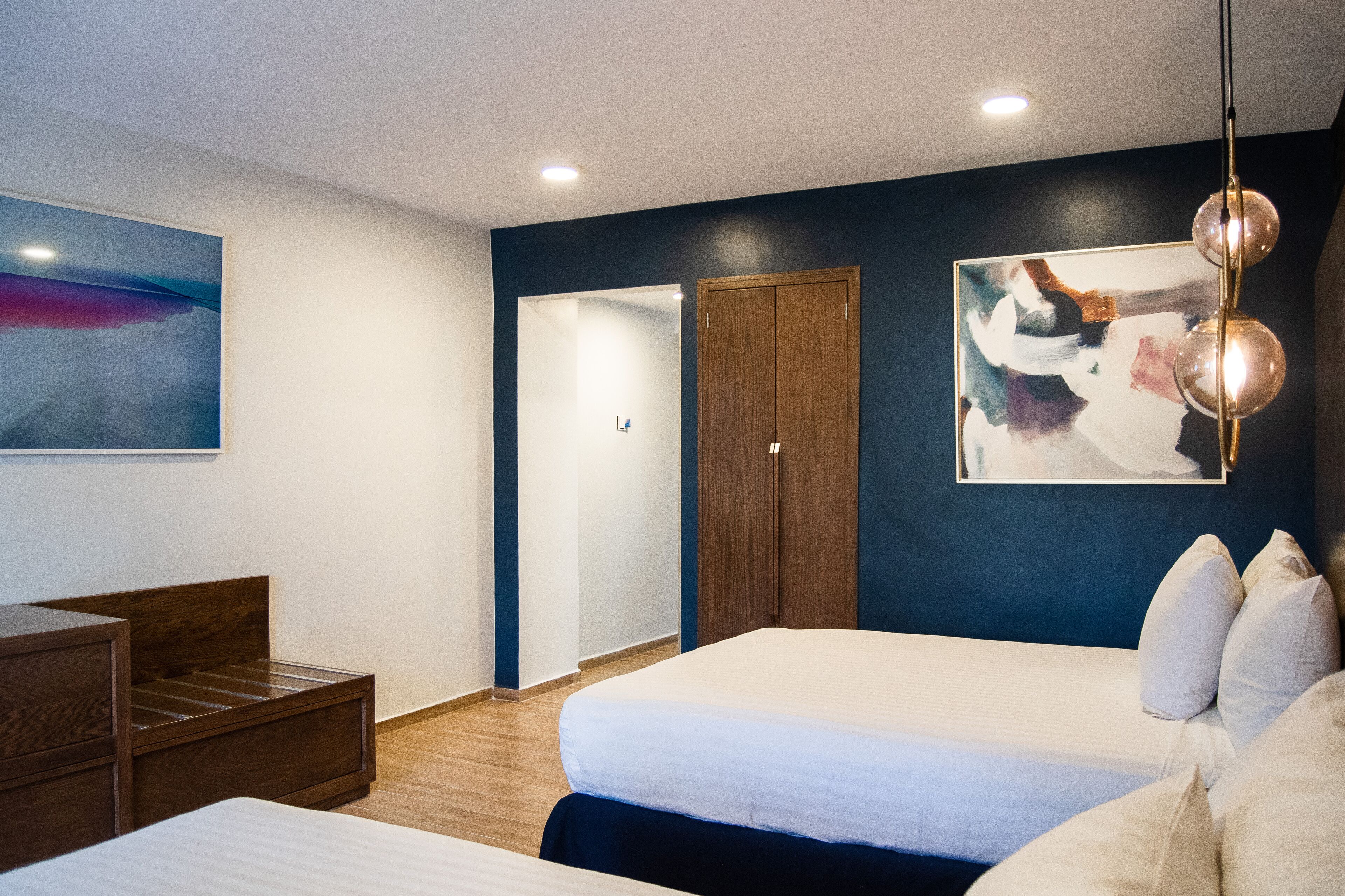 A modern hotel room with a large bed, a wooden nightstand, a desk, and a wardrobe.