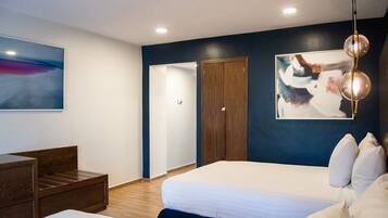 A modern hotel room with a large bed, a wooden nightstand, a desk, and a wardrobe.