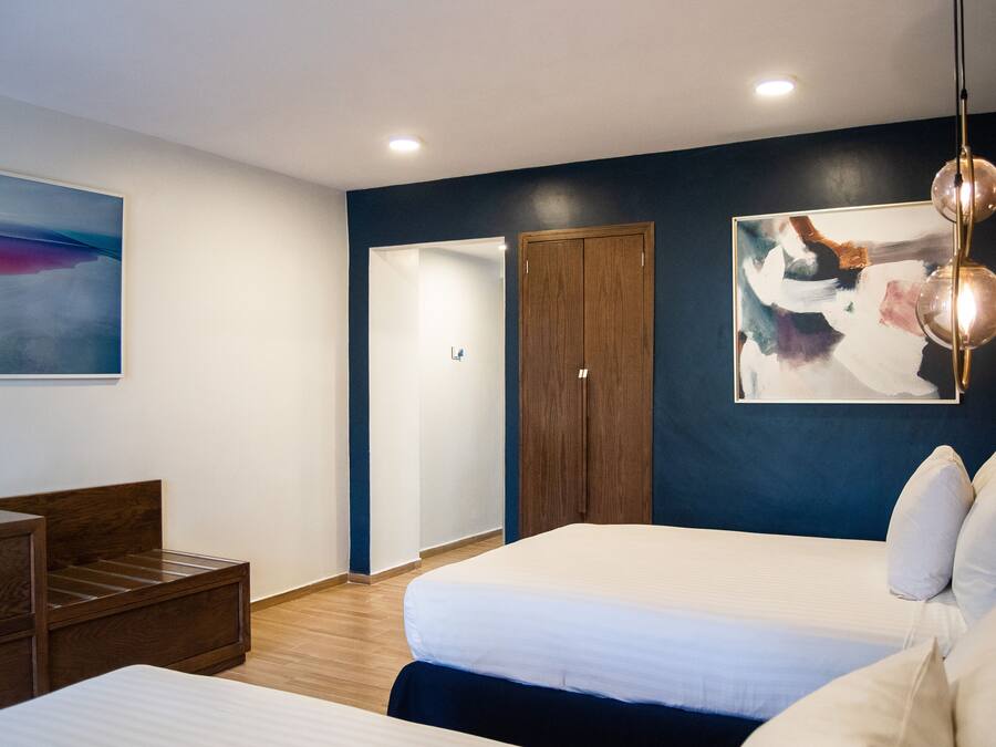 A modern hotel room with a large bed, a wooden nightstand, a desk, and a wardrobe.