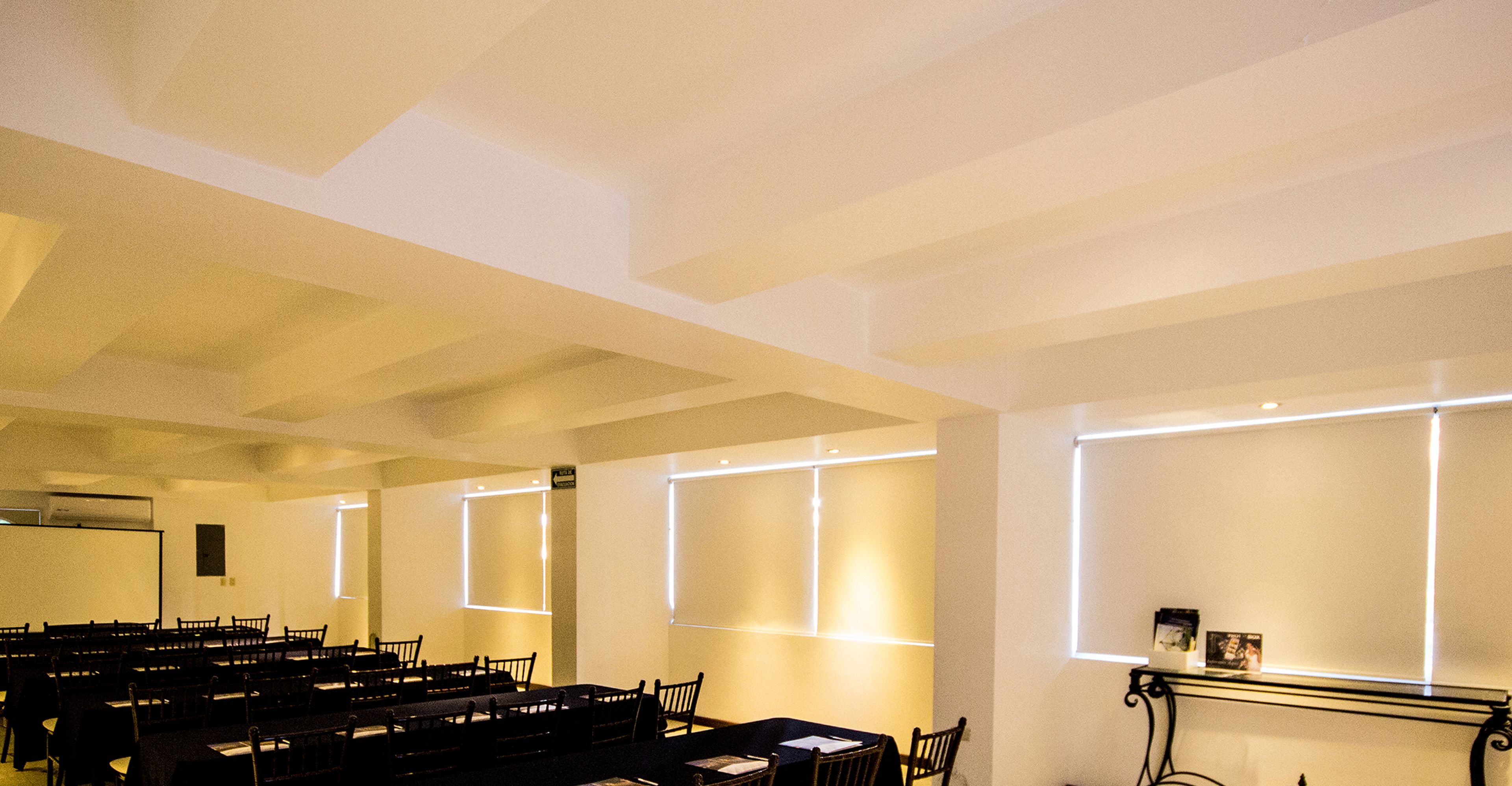 A conference room with rows of tables and chairs, a projector screen, and illuminated wall panels.