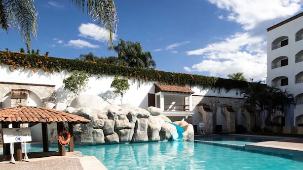 A swimming pool with a rocky feature, a lifebuoy, and a sign indicating a lifeguard on duty. - Gran Plaza Hotel & Convention Center (Guanajuato)