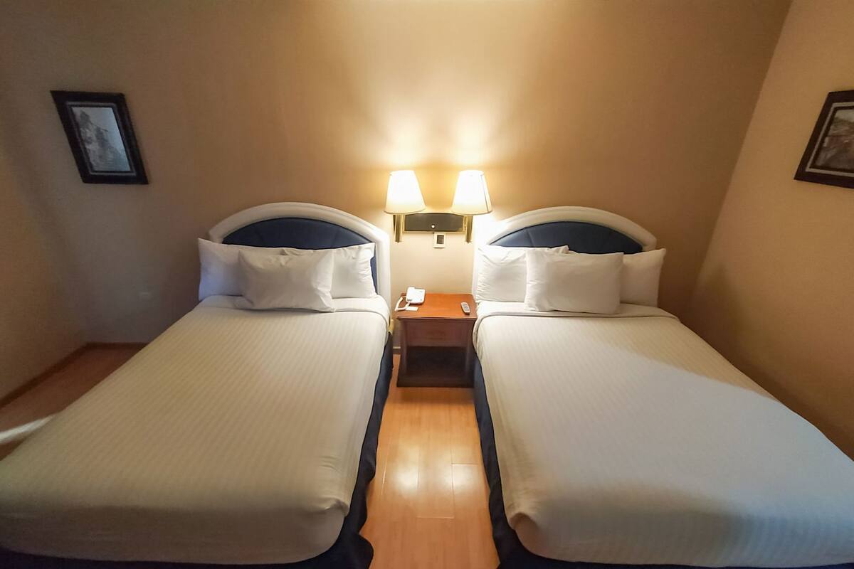 Une chambre double avec deux lits, des lampes de chevet, une table de chevet et un tableau encadré au mur.