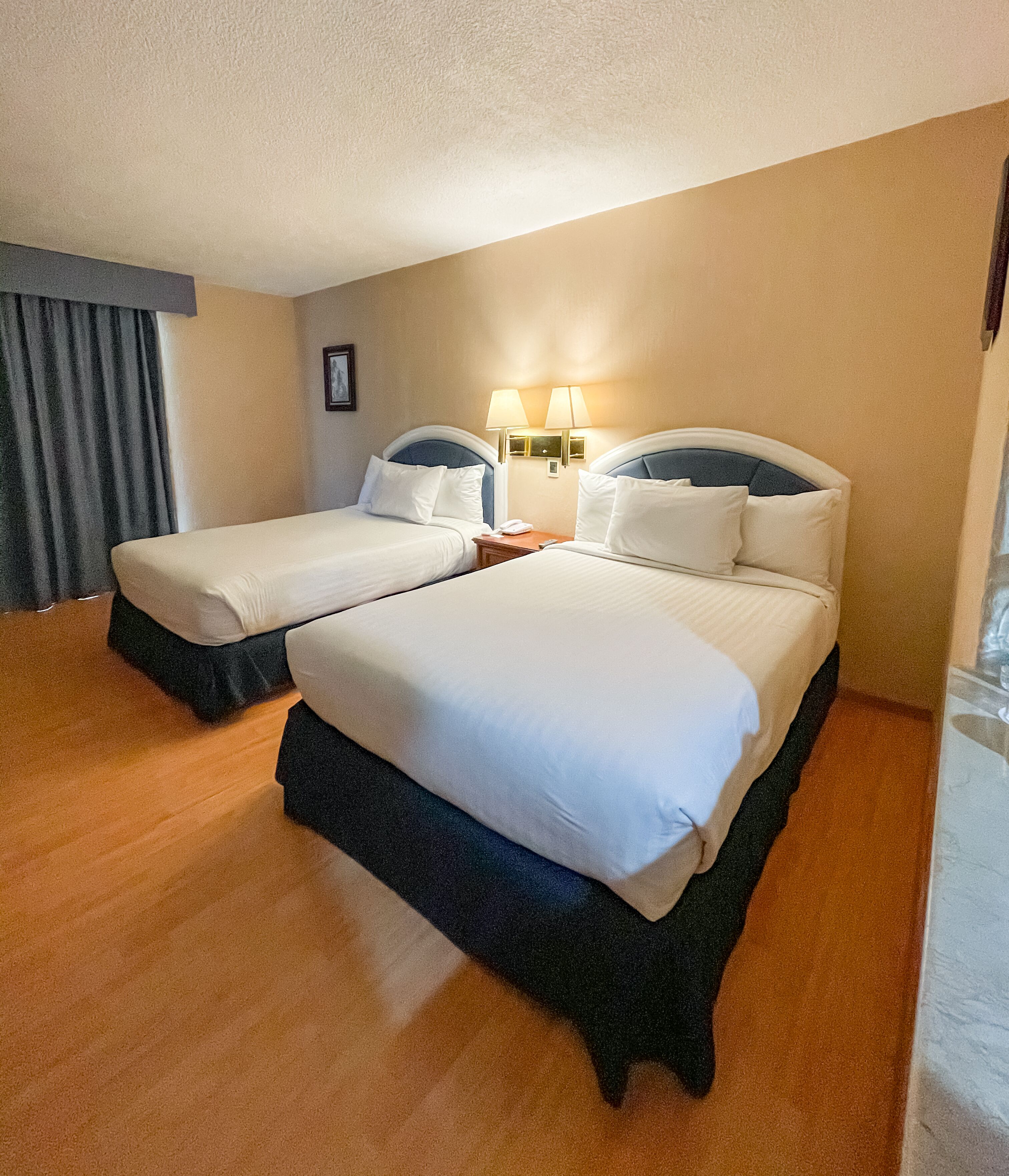 Una habitación de hotel con dos camas, una mesita de noche, una lámpara y una cortina.