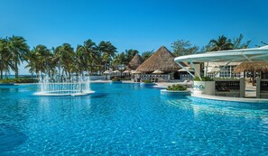 A swimming pool with a fountain, palm trees, and thatched-roof structures. - Catalonia Royal Tulum  Adults Only - All Inclusive (Xpu-Ha)