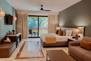 A hotel room with a bed, a desk, a sofa, a ceiling fan, and a view of the outdoors.