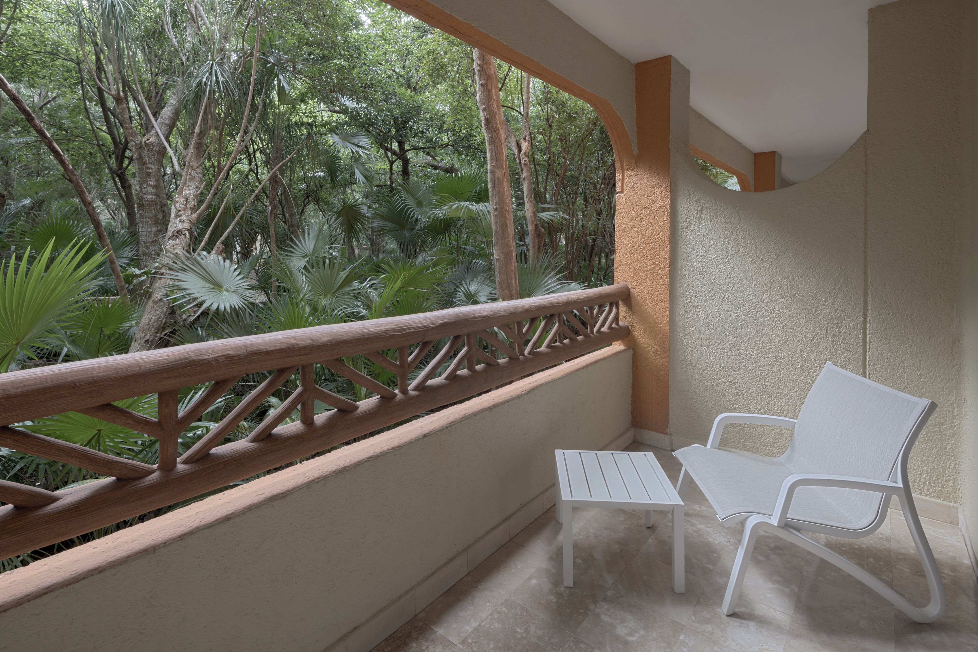 A balcony with a wooden railing, a white table, and a white chair.