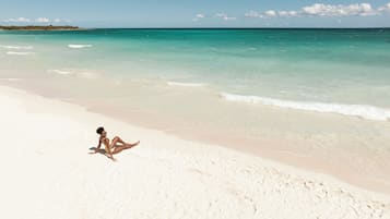 Una persona sentada en una playa de arena con agua turquesa cristalina y una costa distante.