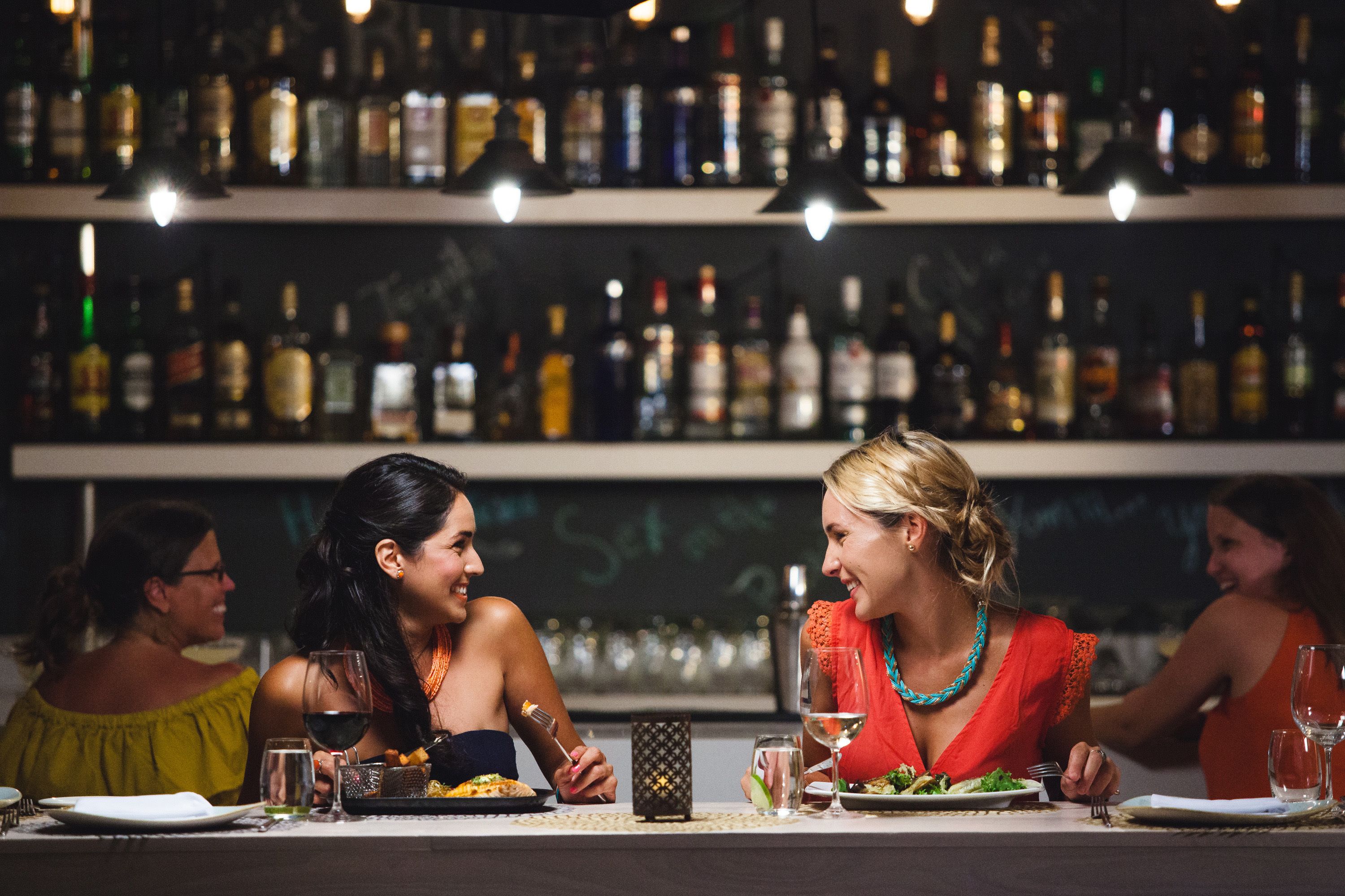 A bar with shelves of bottles and a group of people dining at a table.
