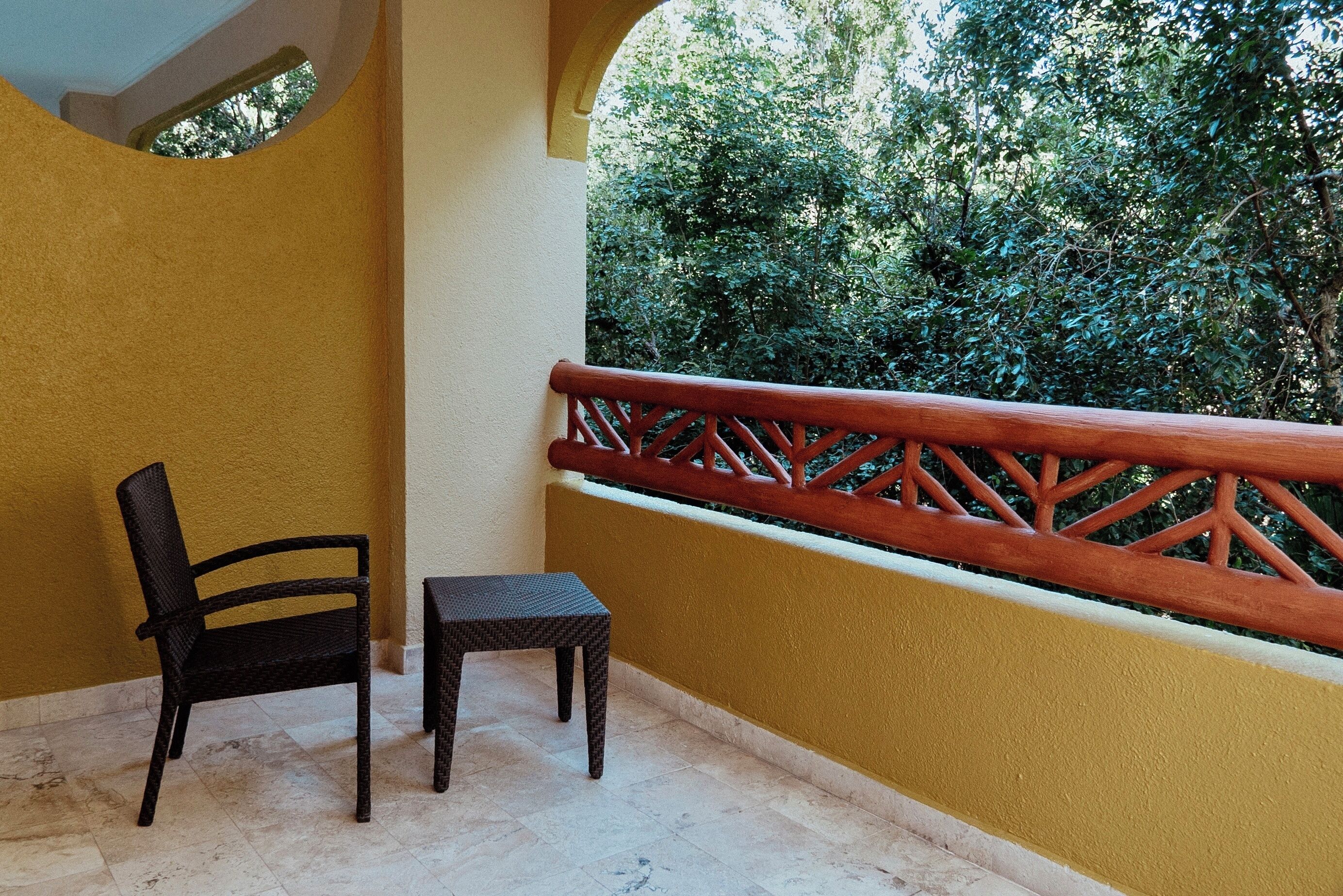 Un balcon avec une chaise et une table, des murs jaunes et une vue sur la verdure.
