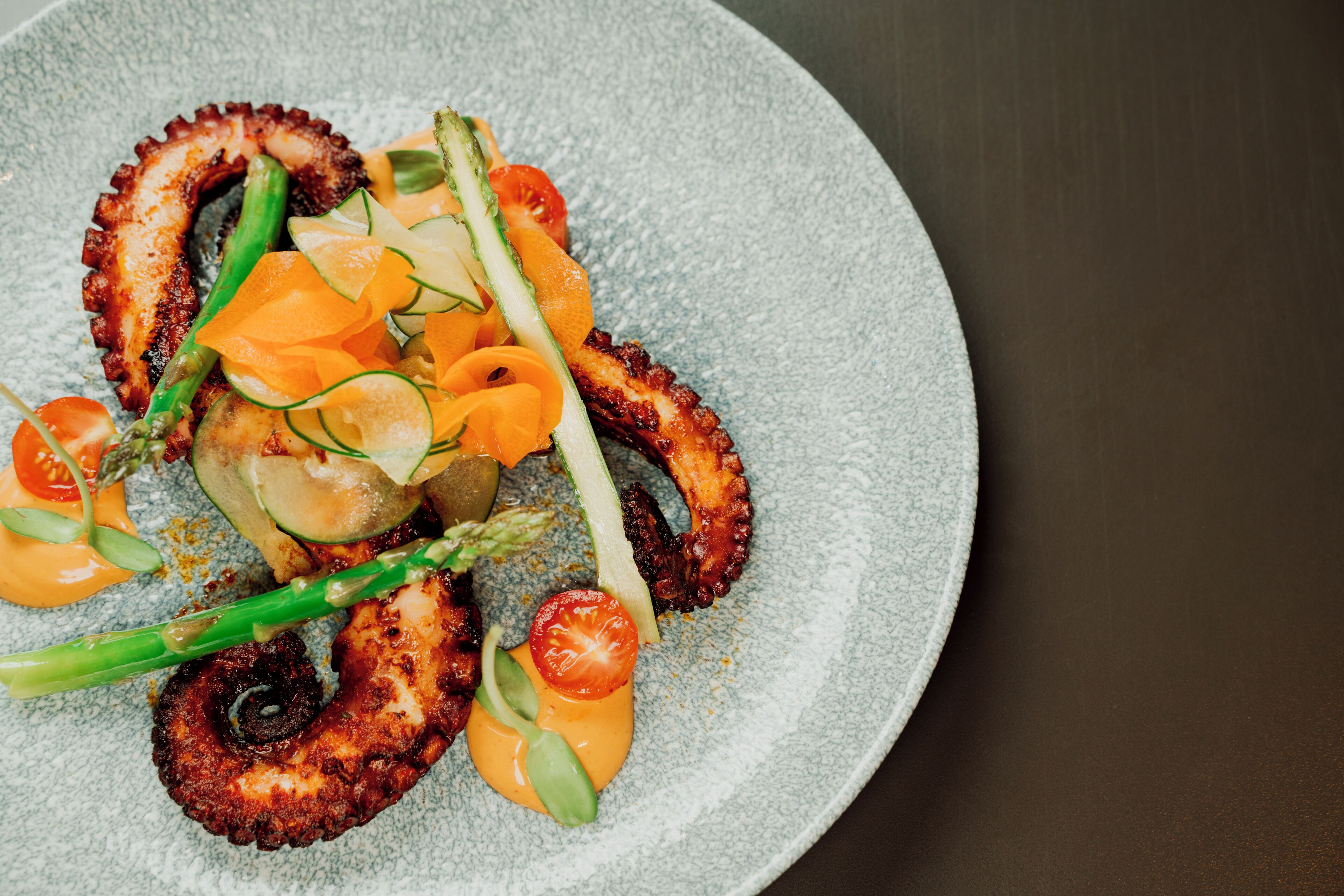 Un plato de comida con pulpo, espárragos y tomates cherry.