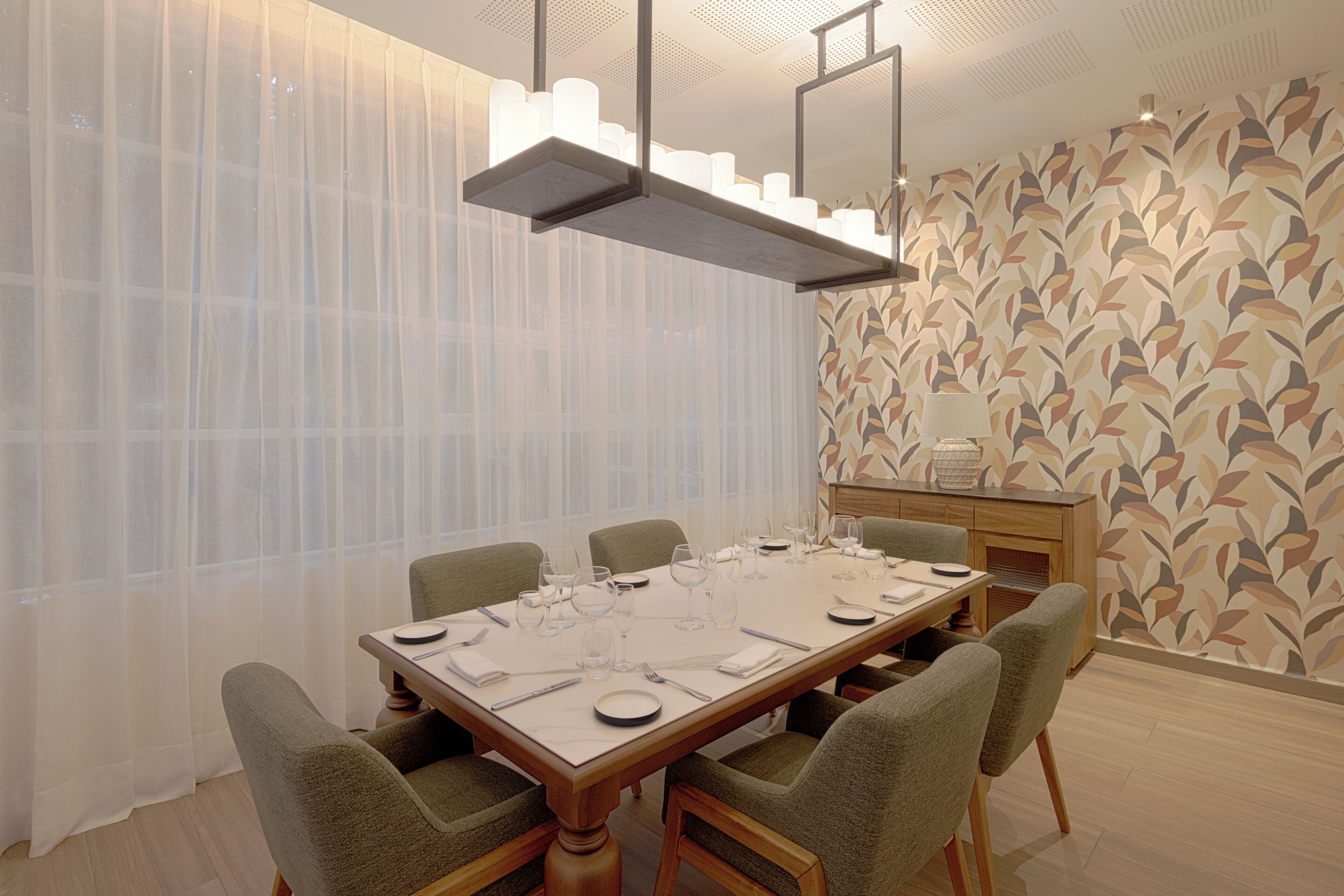 A dining area with a long table set for six, chairs, a chandelier, and a patterned wall.