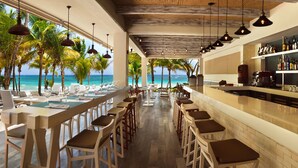 A bar area with a view of the ocean, bar stools, and a shelf with bottles. - Catalonia Royal Tulum  Adults Only - All Inclusive (Xpu-Ha)