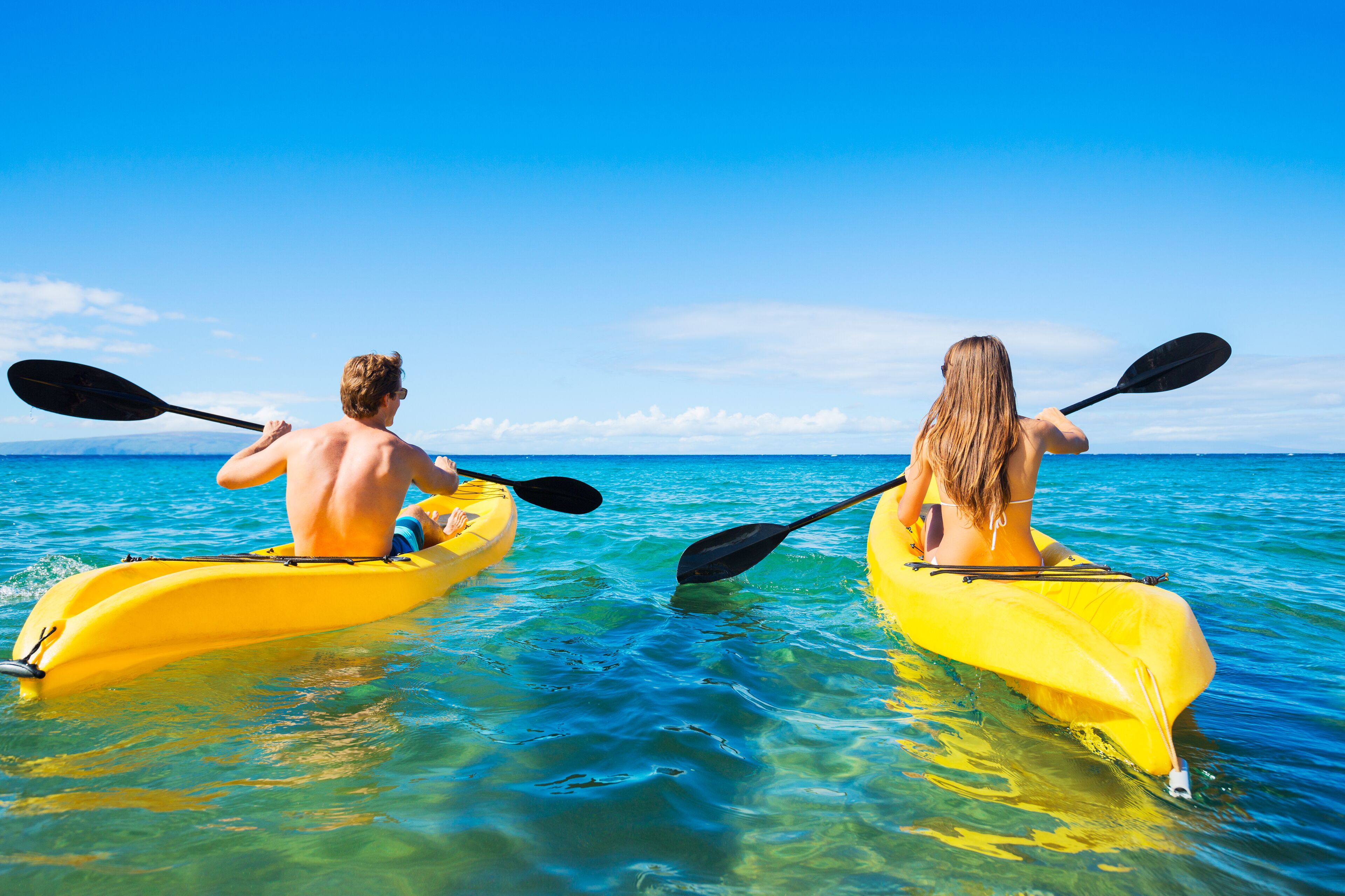 Dos personas haciendo kayak en un mar azul cristalino.