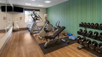 A gym with exercise equipment, a bench, and a rack of dumbbells.