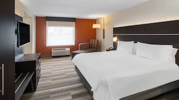 A hotel room with a large bed, a flat-screen TV, a desk, and a window with blinds.