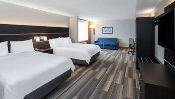 A hotel room with two beds, a desk, a chair, a TV, and a sofa.