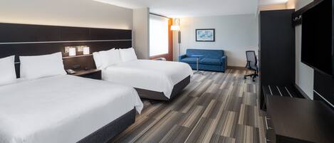 Ett hotellrum med två sängar, ett skrivbord, en stol, en tv och en soffa.