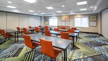 Une salle de conférence équipée de tables et de chaises, recouverte d’un tapis à motifs et ornée d’œuvres d’art encadrées sur les murs.