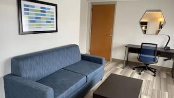 Ein Zimmer mit einem blauen Sofa, einer Holztür, einem Schreibtisch mit Stuhl und einem gerahmten Bild an der Wand.