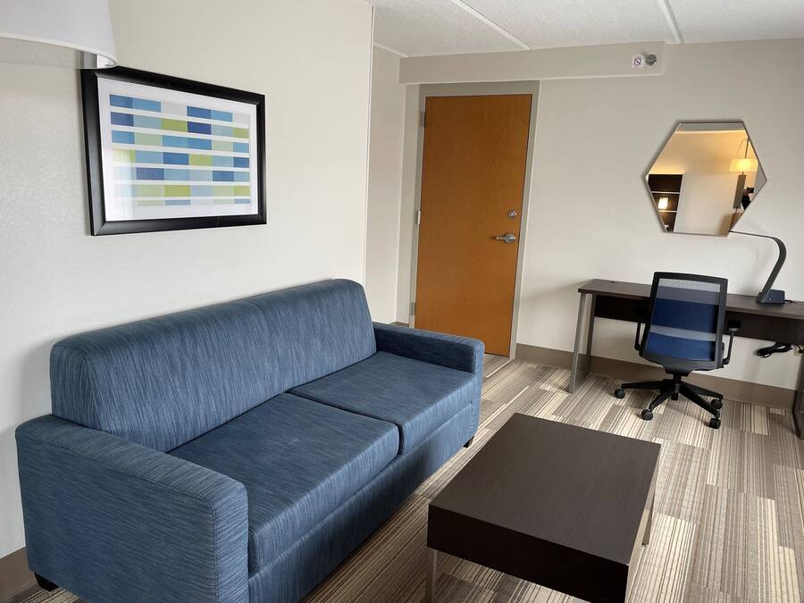 Ein Zimmer mit einem blauen Sofa, einer Holztür, einem Schreibtisch mit Stuhl und einem gerahmten Bild an der Wand.