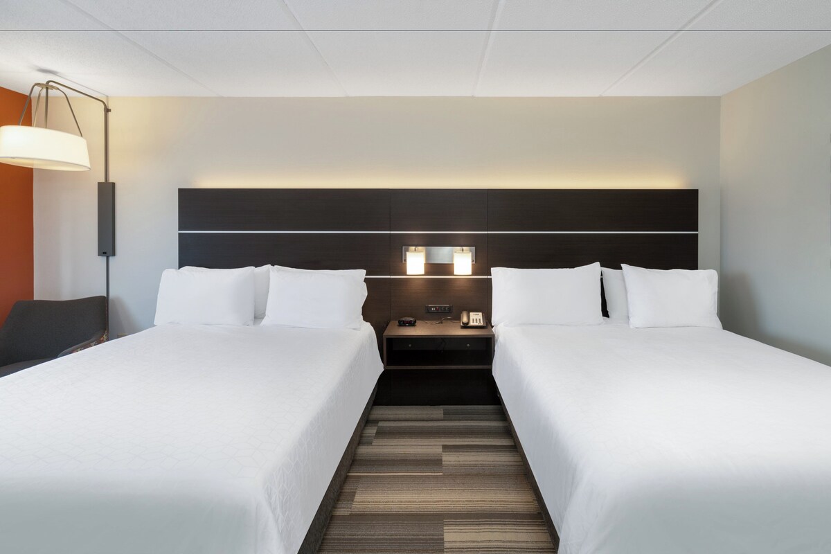 Une chambre d’hôtel avec deux lits, une table de chevet, une lampe et une tête de lit dotée d’un éclairage intégré.