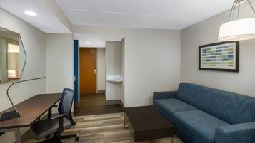 Una habitación de hotel moderna con un escritorio de madera, un sofá azul, una pequeña mesa de centro y un espejo grande.