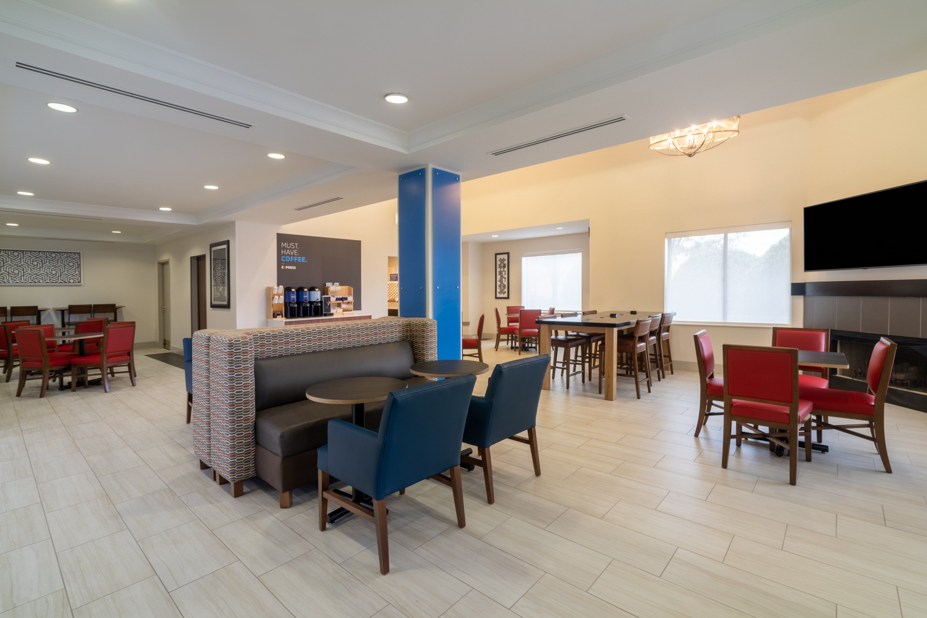 A spacious hotel lobby with a central seating area, a bar, and a television mounted on the wall.