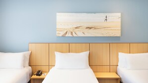 Ein Hotelzimmer mit zwei Betten, einem Holz-Kopfteil, einem Nachttisch mit Telefon und einem Bild mit Strandmotiv.