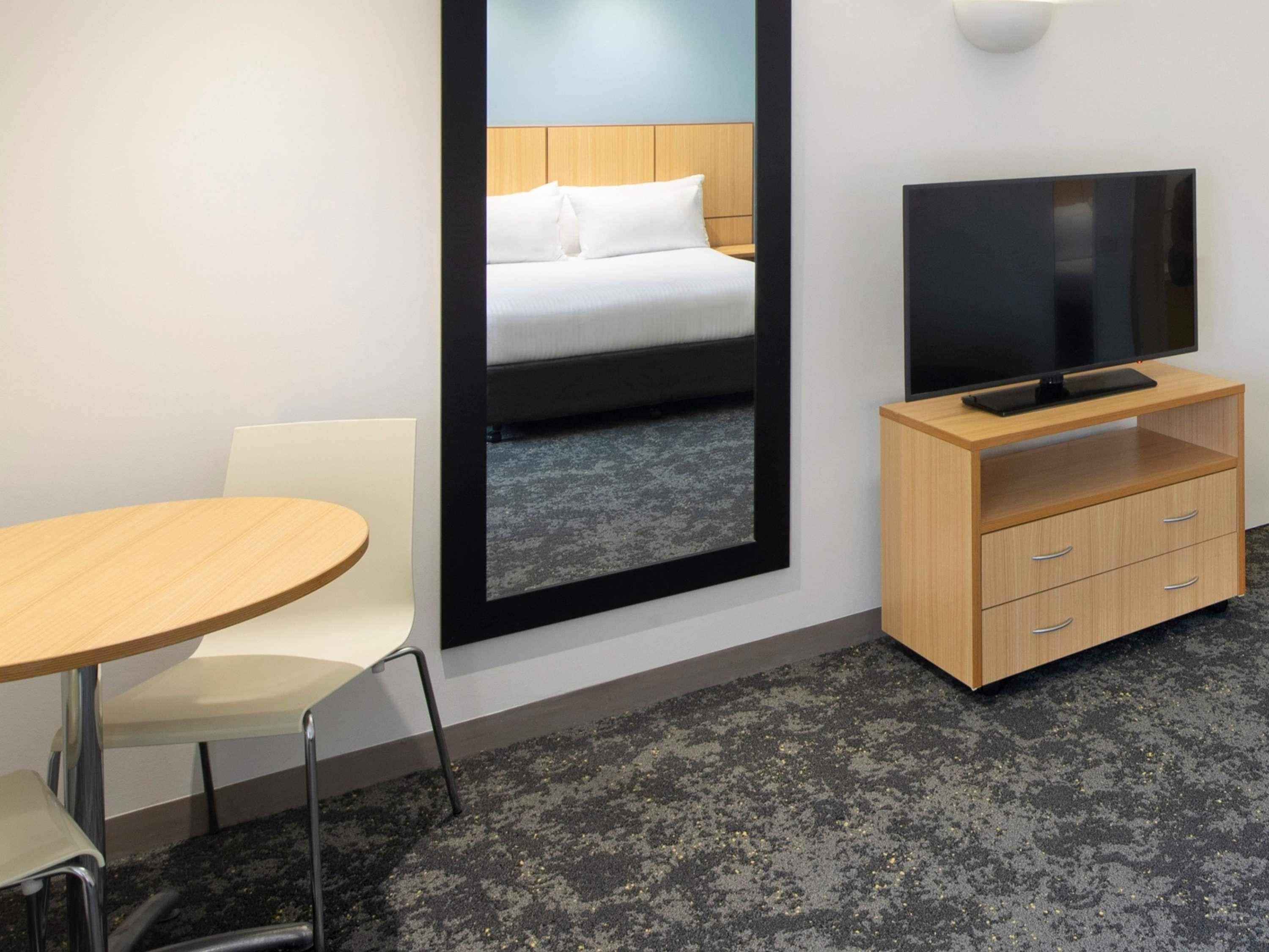 Una habitación de hotel con una cama, un televisor sobre un mueble de madera, una mesa redonda y una silla.