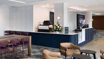 A hotel lobby with a reception desk, seating area, and a coffee machine.
