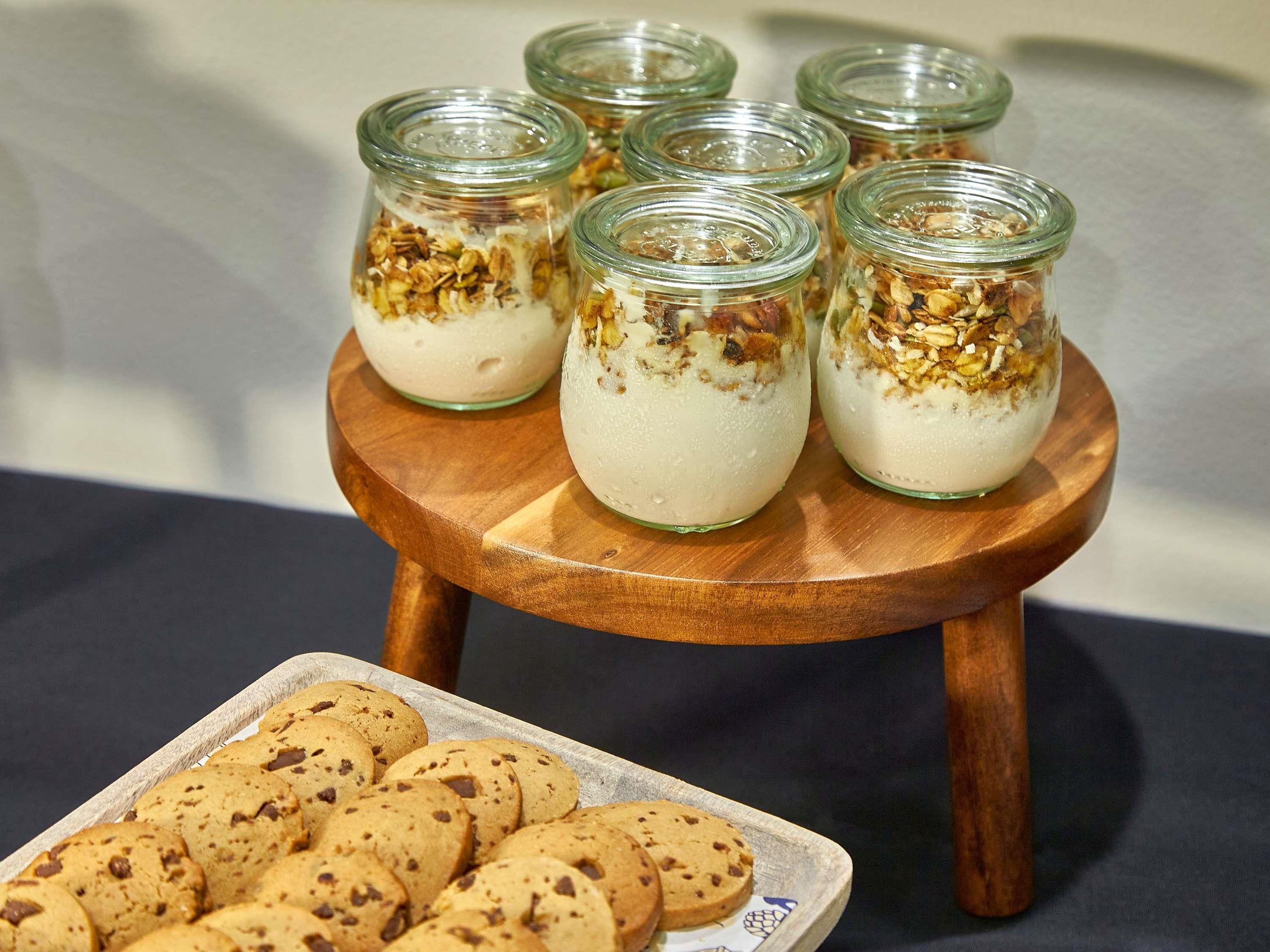A wooden stand with glass jars containing a dessert topped with granola, and a tray of cookies.
