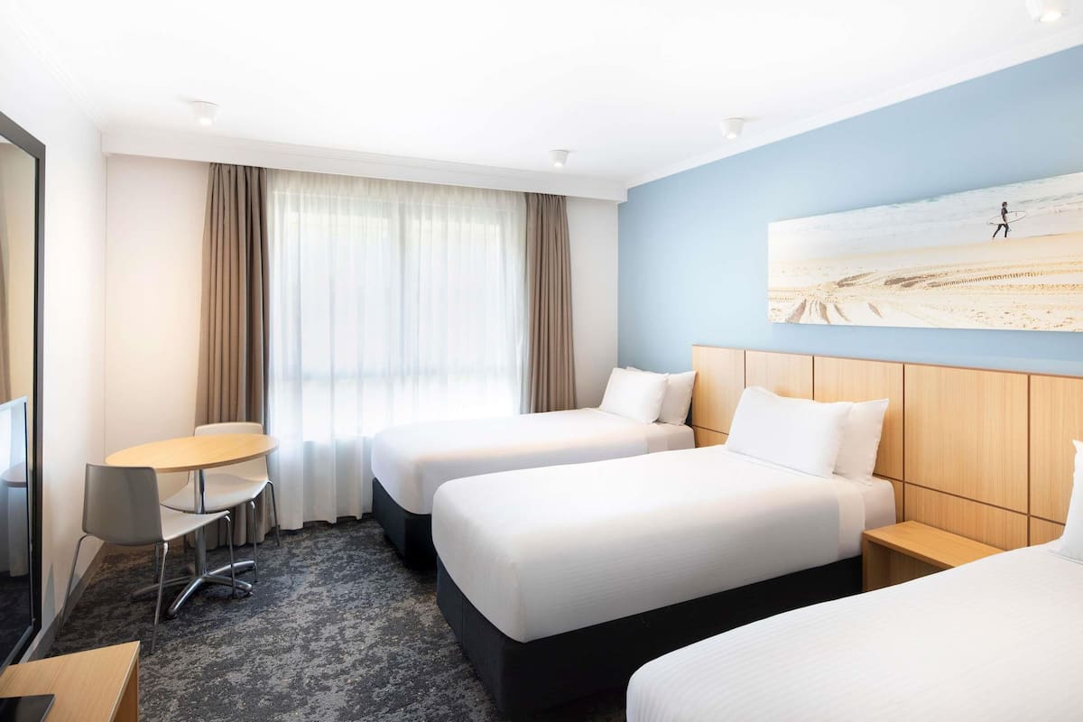 Een hotelkamer met twee bedden, een bureau, een stoel en een groot raam met gordijnen.