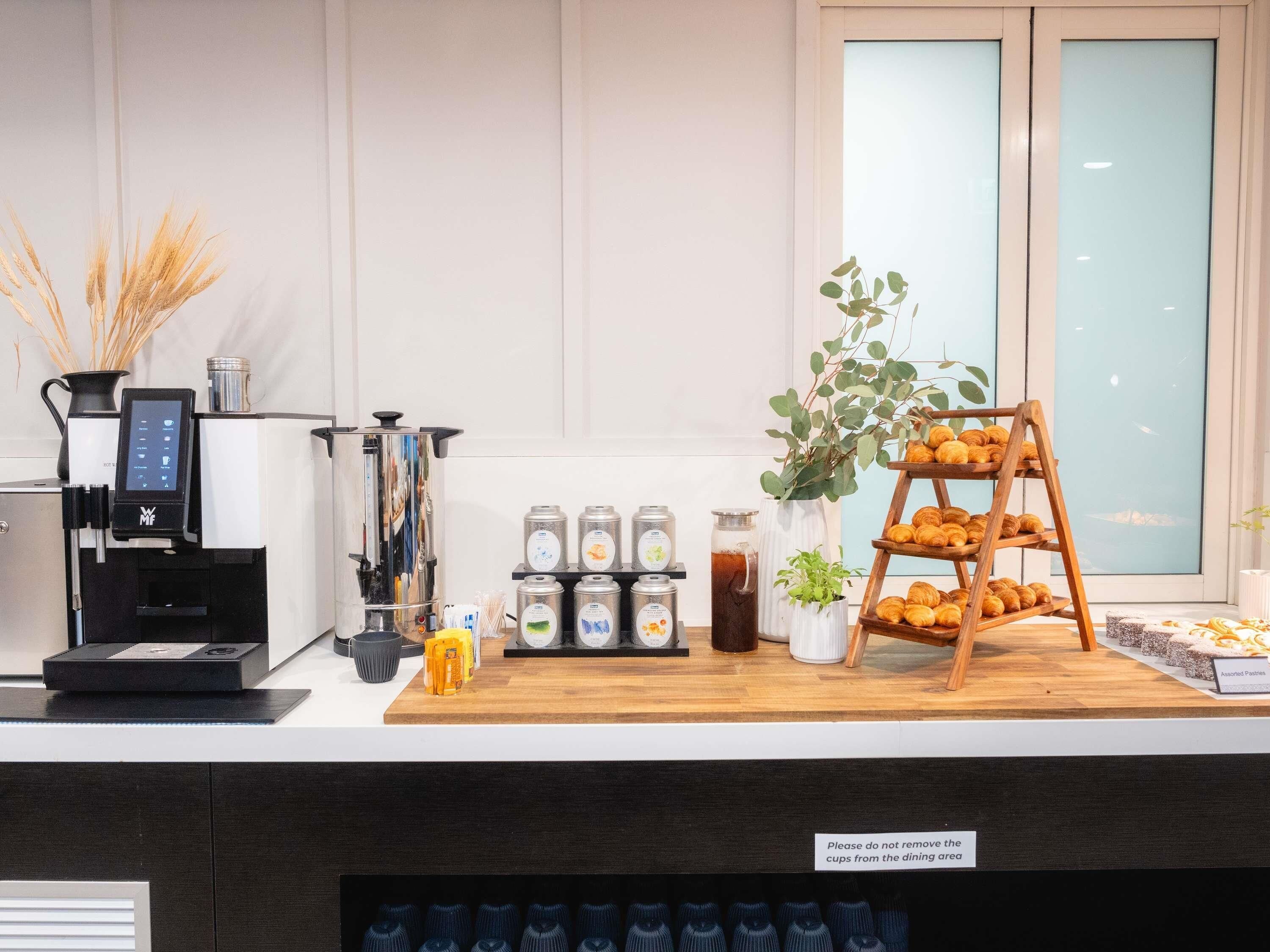 Un coin café équipé d’une machine à café, de pots de crème et d’un présentoir de viennoiseries.