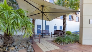 Eine Terrassenanlage im Freien mit großem Sonnenschirm, Sitzgelegenheiten und einem kleinen Garten mit Steinen und Pflanzen.