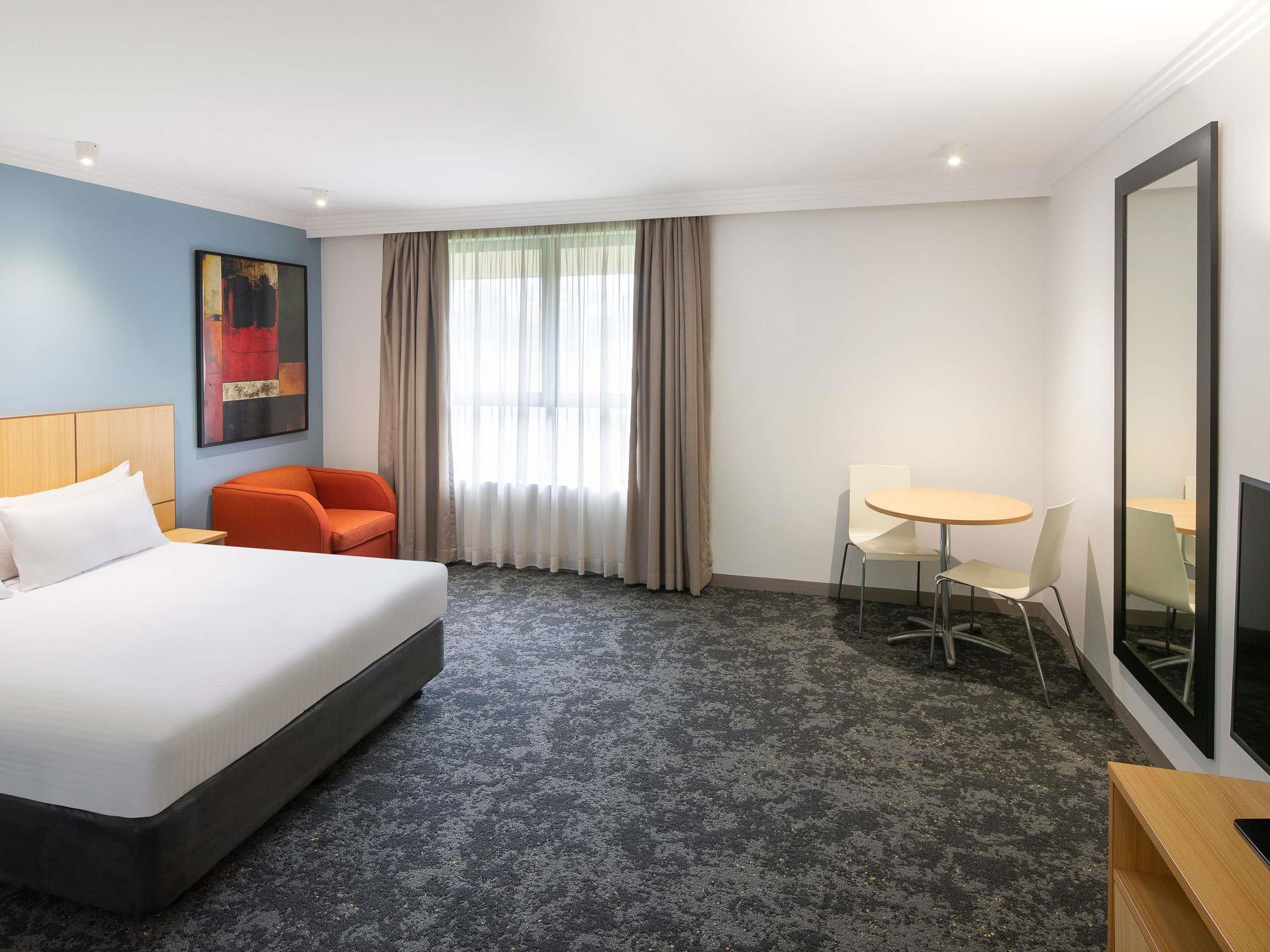 A hotel room with a bed, a desk, a chair, a TV, and a window with curtains.