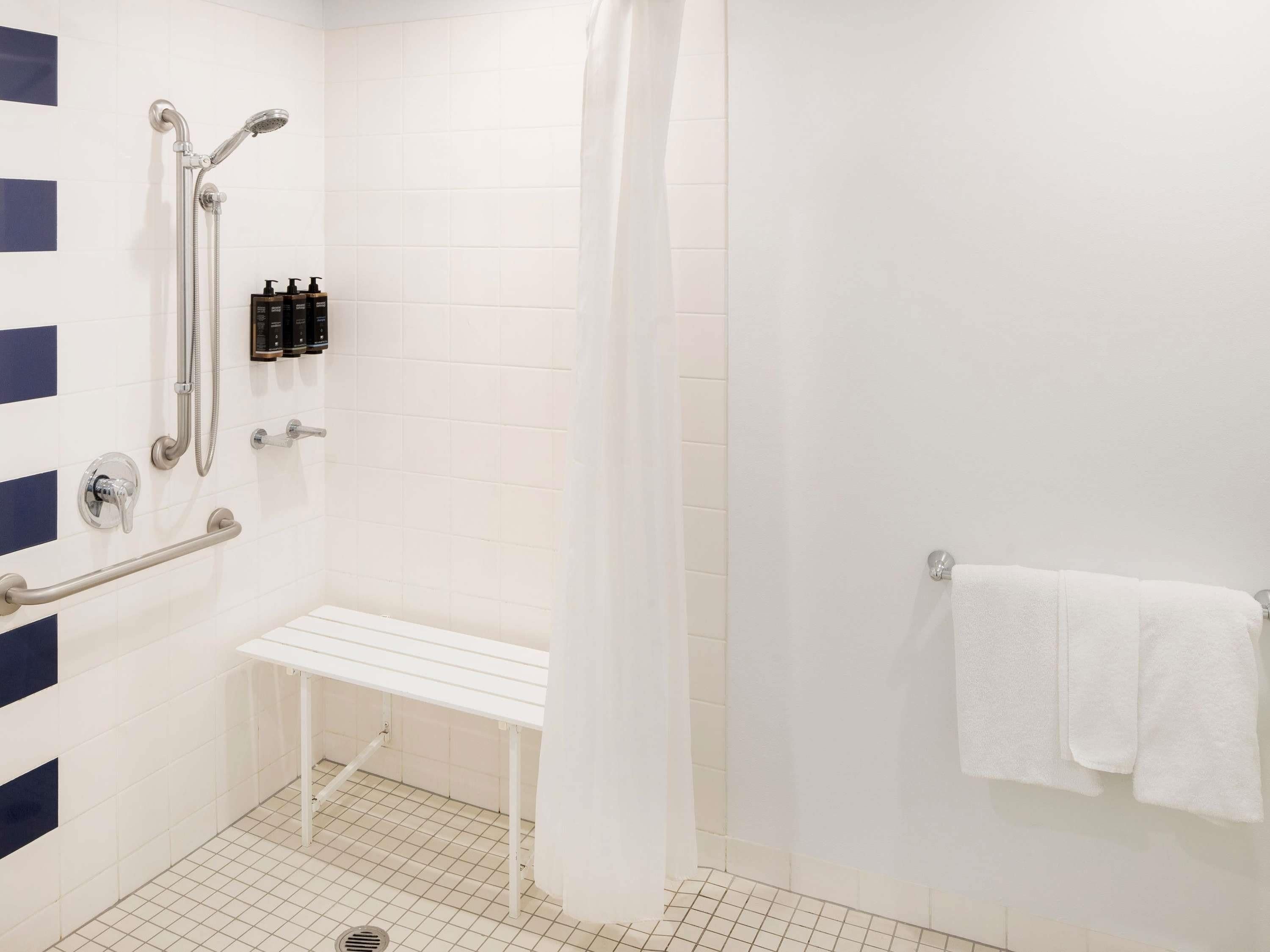 Un baño con ducha, banco, barras de apoyo y un perchero para toallas.