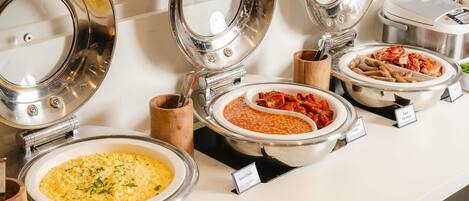 A buffet with labeled dishes including scrambled eggs, baked beans, tomato soup, and sausage.