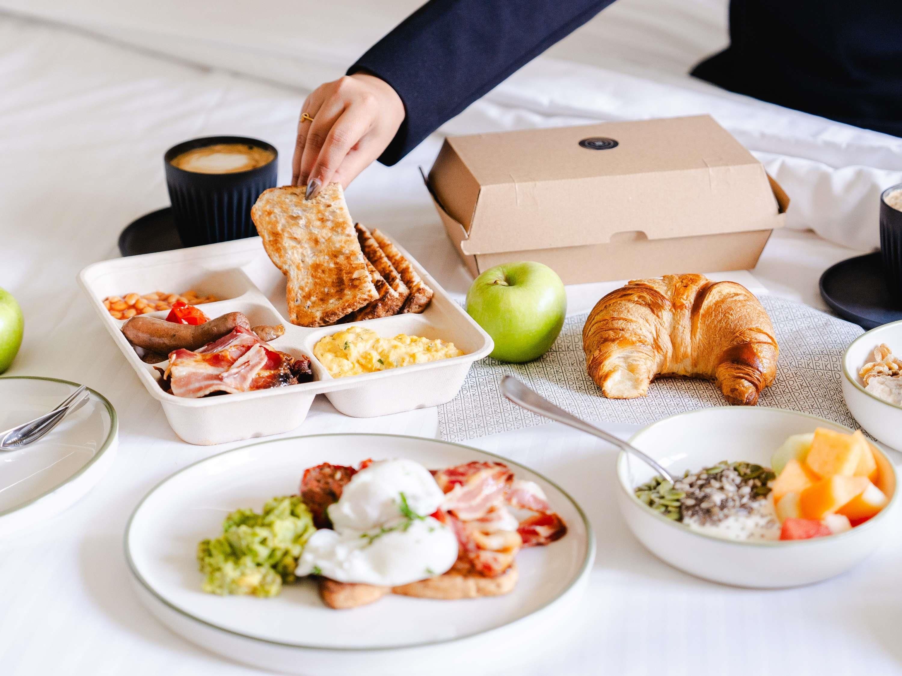 A breakfast spread with toast, eggs, bacon, and a croissant on a bed.