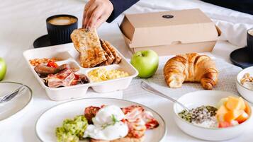 A breakfast spread with toast, eggs, bacon, and a croissant on a bed.